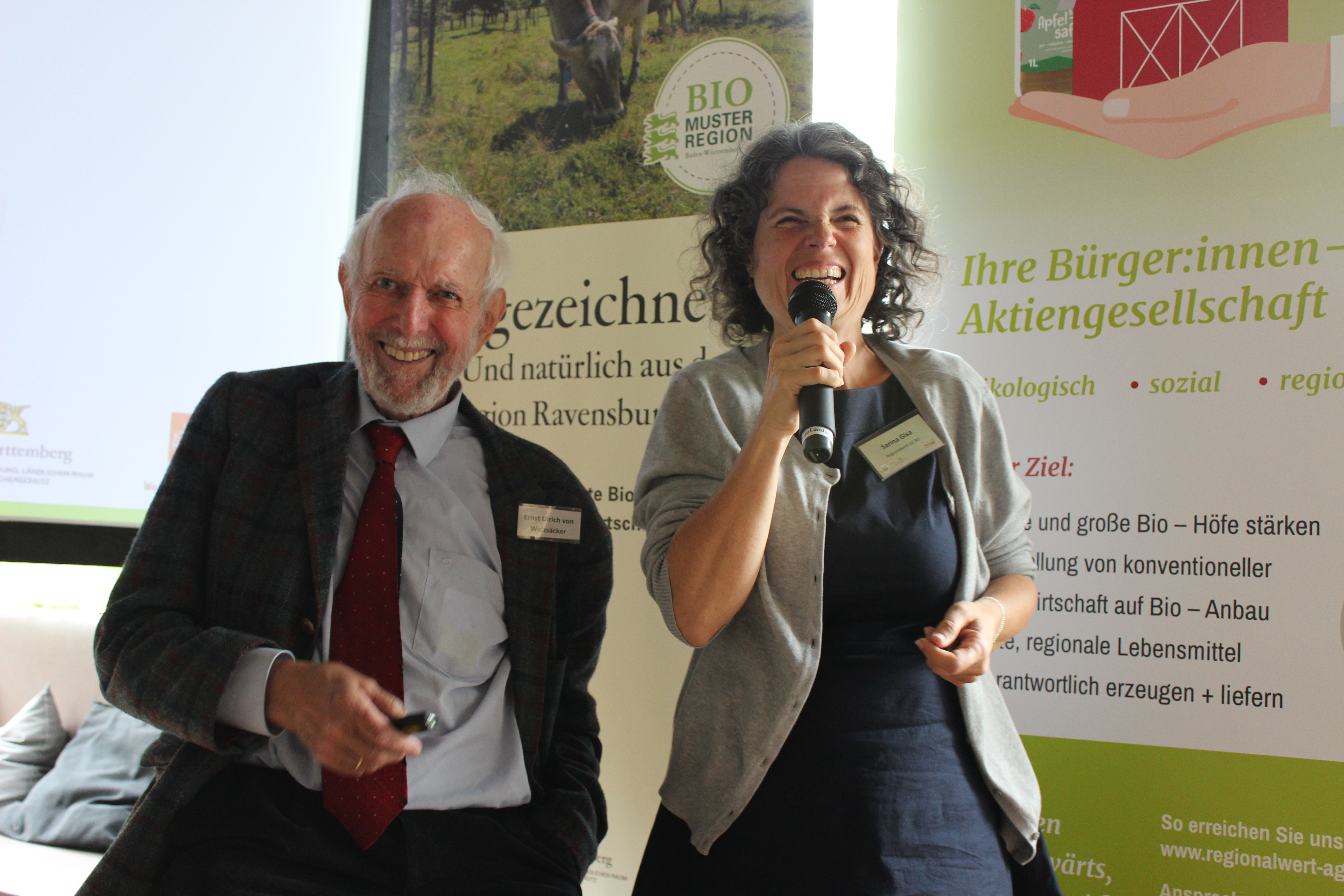 Sarina Gisa (rechts) hält lachend das Mikrofon. Neben ist sieht man Professor Ernst Ulrich von Weizsäcker ebenfalls lachend. 