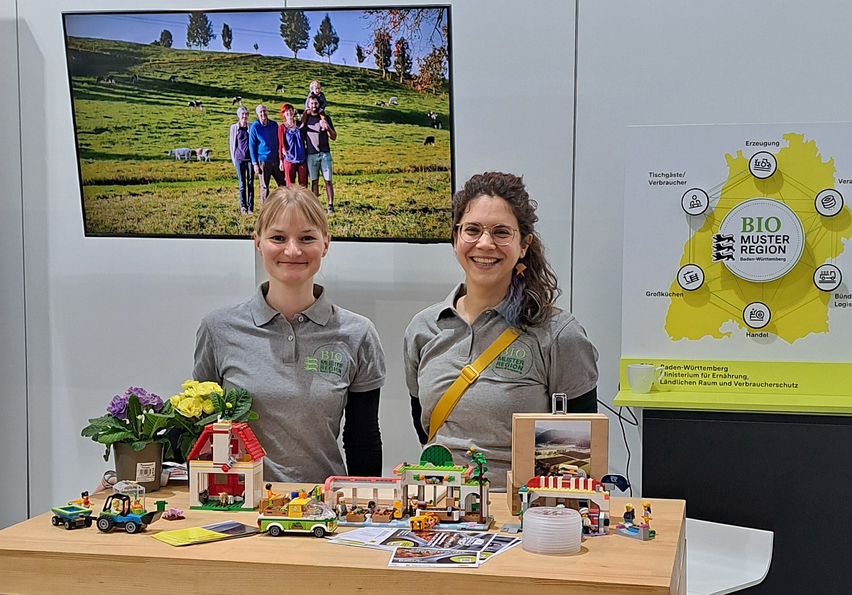 Stand der Biomusterregionen; Foto: C.Rutz Zwei Junge Frauen hinter einem Messestand mit Playmobillandwirtschaft