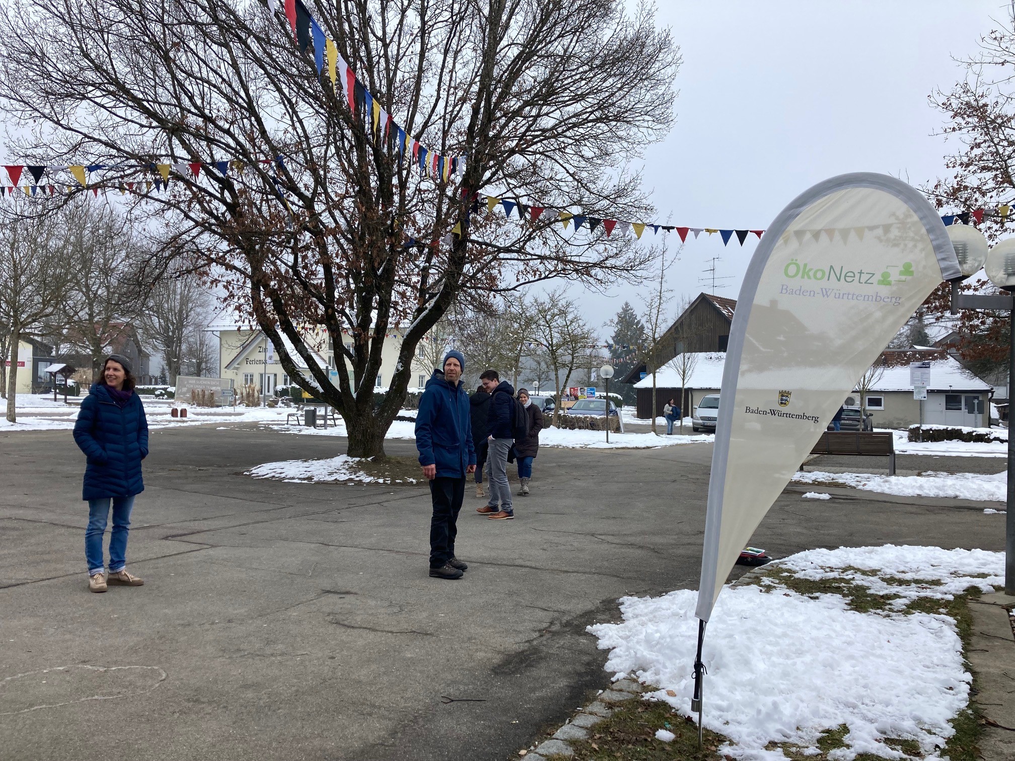 Kleine Personengruppe, im Vordergrund die ÖkoNetzBW-Fahne, in der Hofmitte ein ausladender Baum